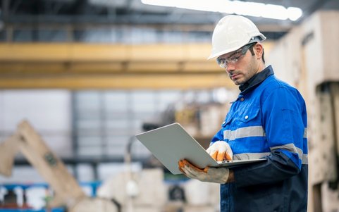 Occupational safety professional wearing a white helmet and blue jacket, using a laptop