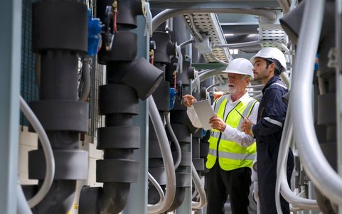 Two health and safety specialists wearing a white helmet, using a tablet.