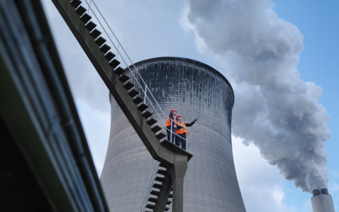 Two employees wearing orange vests in front of a coal power plant
