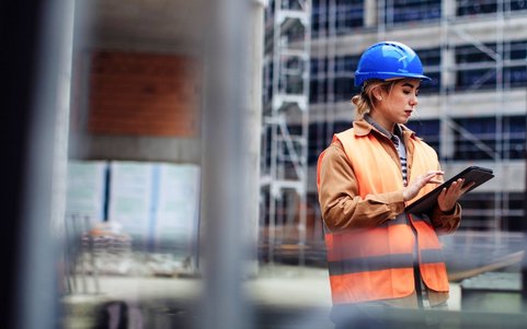 A occupational safety professional with a blue helmet, using an EHS app on a tablet